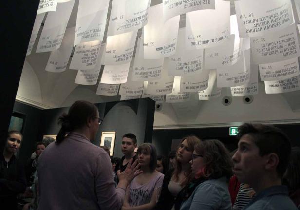 Eine Gruppe von Menschen betrachtet eine Kunstinstallation mit hängenden Papierbögen.