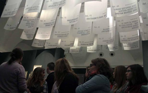 Besucher betrachten eine Installation mit von der Decke hängenden Blättern mit Text.