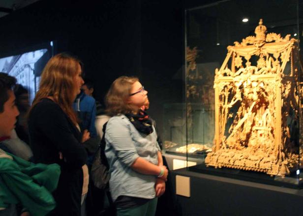 Besucher betrachten ein aufwendig geschnitztes, goldenes Kunstwerk in einem Museum.