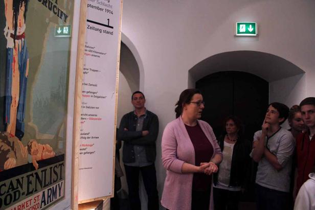 Eine Gruppe von Menschen steht in einem Ausstellungsraum vor einem Plakat und einer Informationstafel.