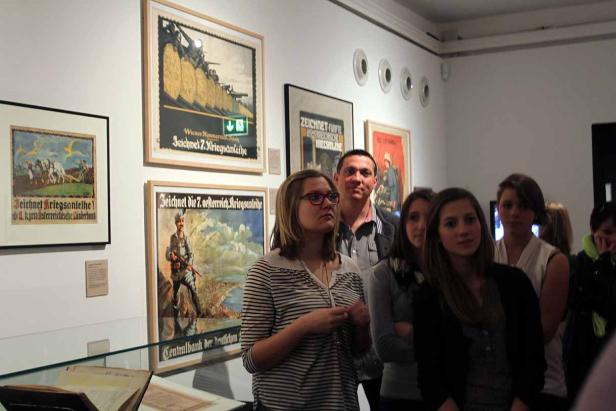 Eine Gruppe von Menschen betrachtet alte Kriegspropaganda-Plakate in einem Museum.