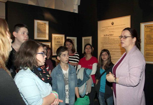 Eine Museumsführerin erklärt einer Gruppe von Jugendlichen und Erwachsenen historische Dokumente.