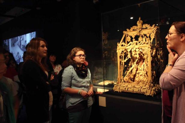 Besucher betrachten ein aufwendig geschnitztes, goldenes Ausstellungsstück in einem Museum.