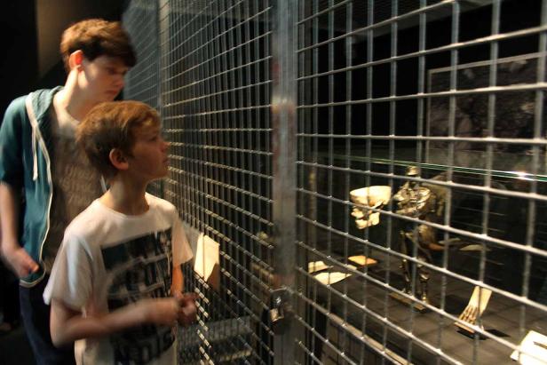 Zwei Jungen betrachten ein Ausstellungsstück mit einem Skelett hinter einem Gitter.