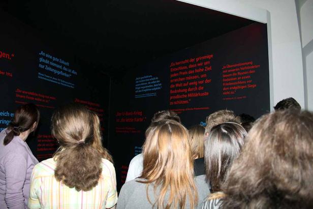 Eine Gruppe von Menschen betrachtet Zitate an einer Wand in einer Ausstellung.