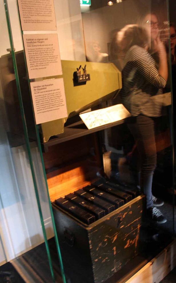Eine Vitrine zeigt einen Behälter mit Kassetten für Glasplatten und ein Faltblatt zu Fliegern.