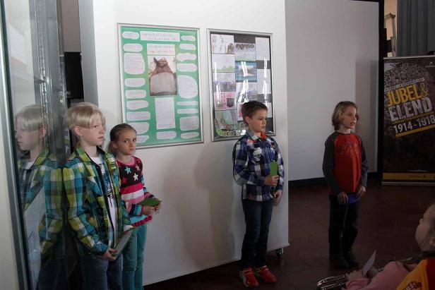 Vier Kinder stehen vor Plakaten in einem Raum.