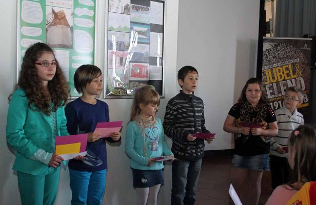 Eine Gruppe von Kindern steht vor einer Wand mit Bildern und einem Plakat für „Jubel & Elend“.