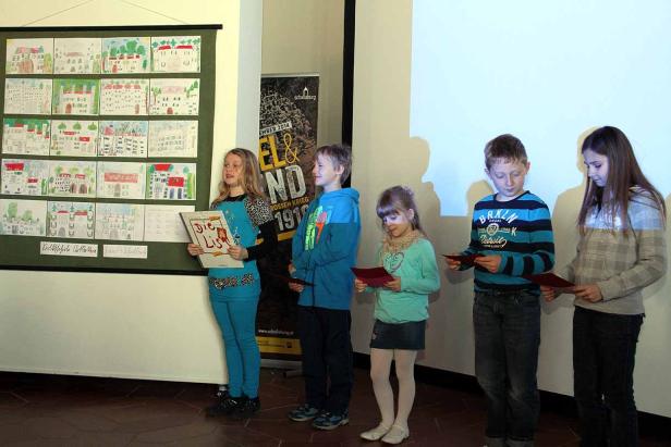 Fünf Kinder stehen vor einer Wand mit Zeichnungen und halten Urkunden.