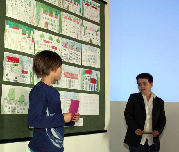 Zwei Jungen stehen vor einer Wand mit Kinderzeichnungen von Häusern.