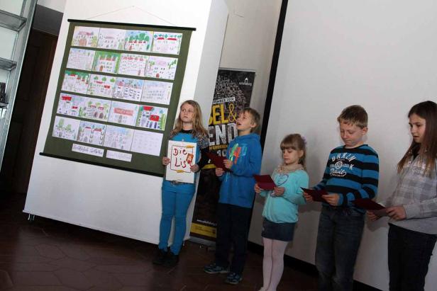 Fünf Kinder stehen vor einer Wand mit Kinderzeichnungen und lesen vor.