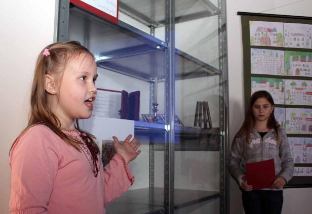 Ein Mädchen präsentiert eine Ausstellung mit Kinderzeichnungen und religiösen Gegenständen.