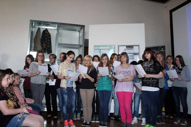 Eine Gruppe junger Frauen steht und liest von Papierblättern.