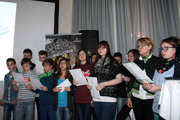 Eine Gruppe von Jugendlichen steht und singt von Papierblättern.