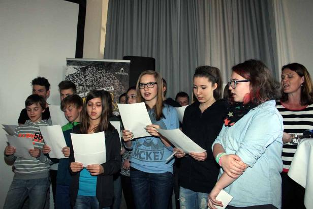 Eine Gruppe von Jugendlichen und Erwachsenen singt gemeinsam aus Notenblättern.