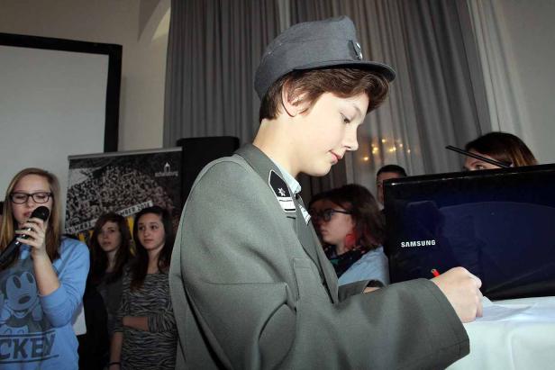 Ein Jugendlicher in Uniform schreibt an einem Tisch, umgeben von anderen Jugendlichen.