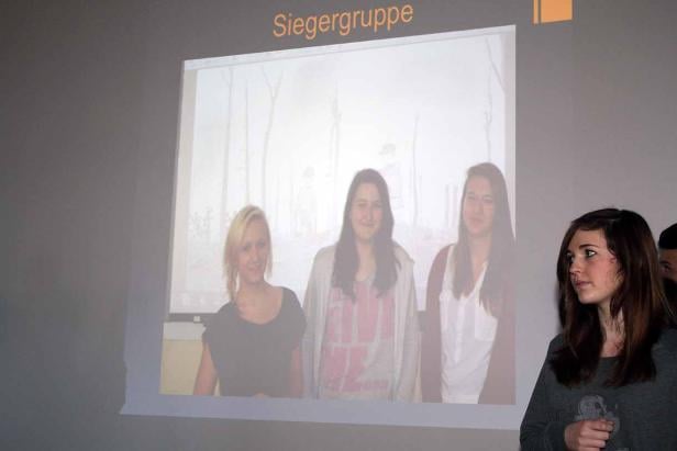 Eine junge Frau steht vor einer Projektion, die drei weitere junge Frauen zeigt.