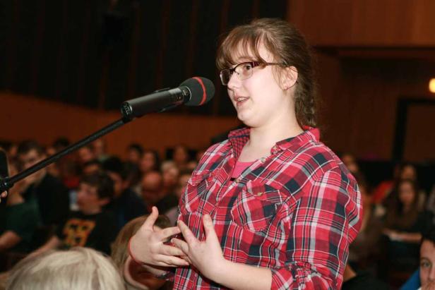 Eine junge Frau spricht bei einer Veranstaltung in ein Mikrofon.