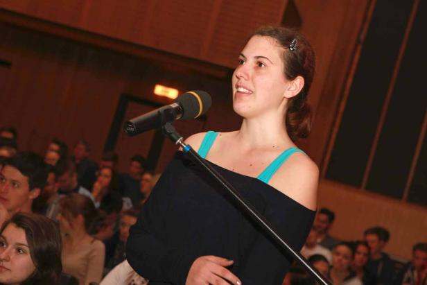 Eine junge Frau spricht vor einem Publikum in ein Mikrofon.
