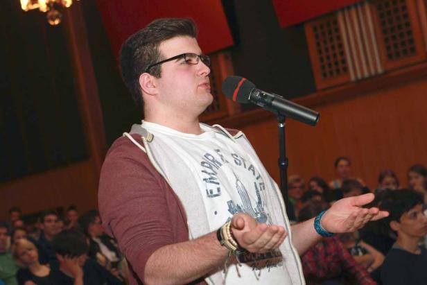Ein junger Mann mit Brille spricht vor Publikum in ein Mikrofon.