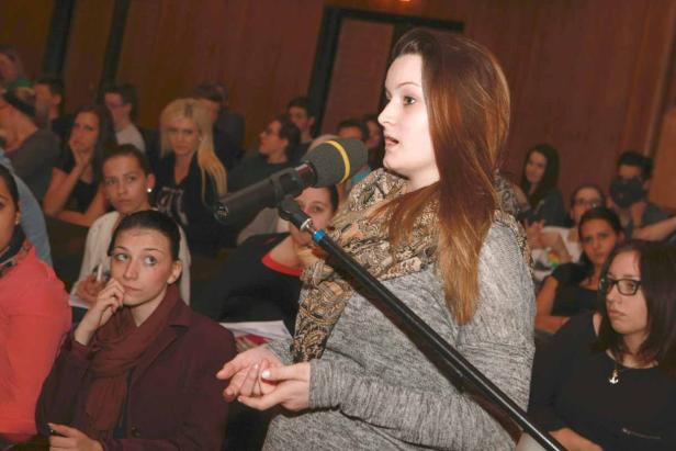 Eine junge Frau spricht bei einer Veranstaltung in ein Mikrofon.