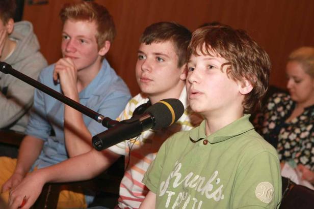 Ein junger Mann spricht in ein Mikrofon, während andere ihm zuhören.