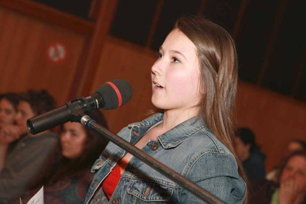 Eine junge Frau spricht in ein Mikrofon vor Publikum.