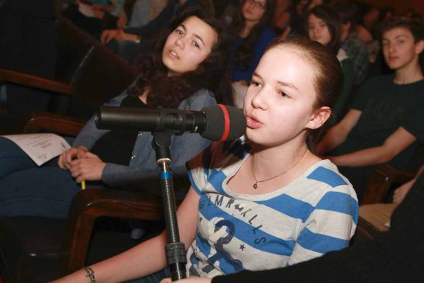 Ein junges Mädchen spricht in ein Mikrofon vor einem Publikum.