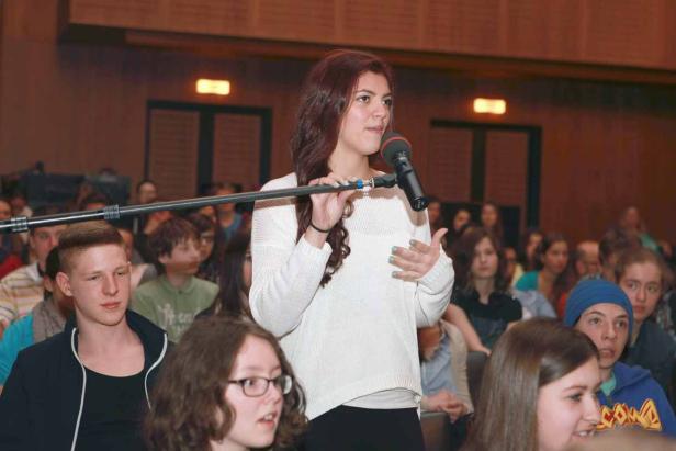 Eine junge Frau spricht bei einer Veranstaltung in ein Mikrofon.