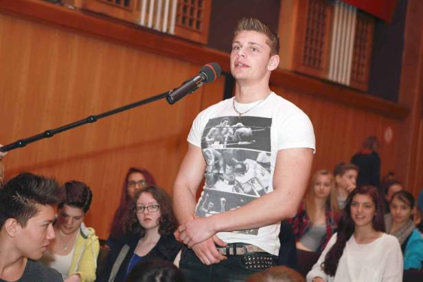 Ein junger Mann spricht vor Publikum in ein Mikrofon.