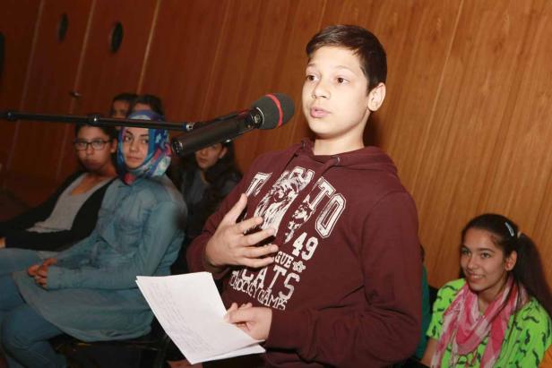 Ein Junge spricht vor einem Mikrofon, während andere ihm zuhören.