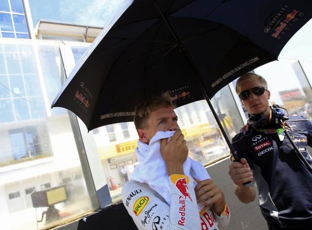 Sebastian Vettel wird von einem Mitarbeiter mit einem Handtuch und einem Regenschirm versorgt.