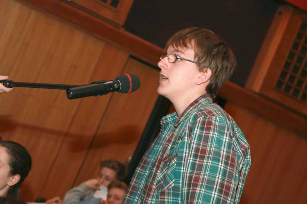 Ein junger Mann mit Brille spricht in ein Mikrofon.