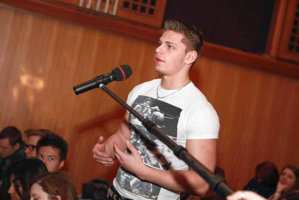 Ein junger Mann spricht bei einer Veranstaltung in ein Mikrofon.