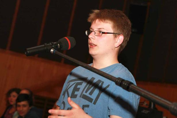 Ein junger Mann mit Brille spricht in ein Mikrofon.