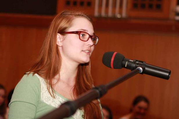 Eine junge Frau mit Brille spricht in ein Mikrofon.