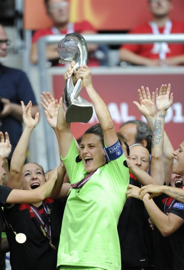Eine jubelnde Fußballspielerin hält den Pokal in die Höhe, umringt von ihren Teamkolleginnen.