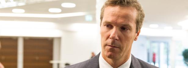 Ein Mann in einem grauen Anzug blickt nachdenklich zur Seite.