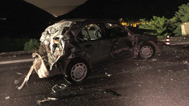Ein schwer beschädigtes Auto steht nachts auf einer Straße.