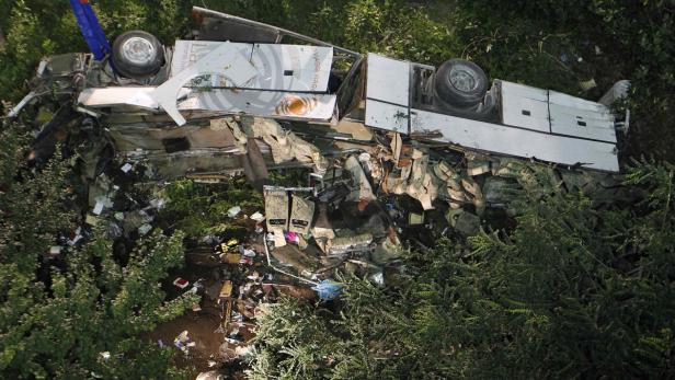 Ein zerstörter Bus liegt auf der Seite, umgeben von Vegetation.