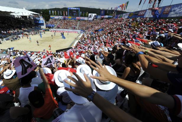 Zuschauer jubeln bei einem Beachvolleyballspiel mit Hüten und Fahnen.