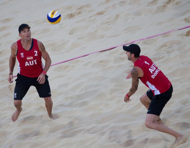 Zwei Beachvolleyballspieler aus Österreich bei einem Spiel im Sand.