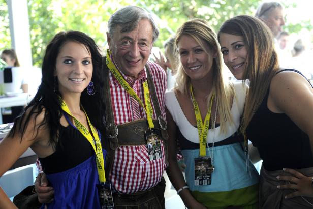 Ein älterer Mann in Tracht posiert mit drei jungen Frauen für ein Foto.