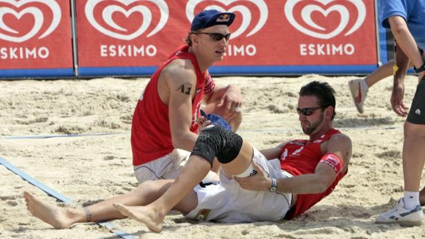 Ein Beachvolleyballspieler wird von seinem Teamkollegen auf dem Spielfeld behandelt.