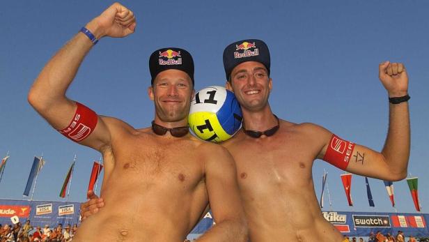 Zwei Beachvolleyballspieler mit Red Bull-Kappen posieren mit einem Ball.