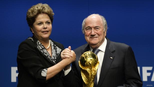 Dilma Rousseff und Sepp Blatter schütteln sich die Hände neben der FIFA-Weltmeisterschaftstrophäe.