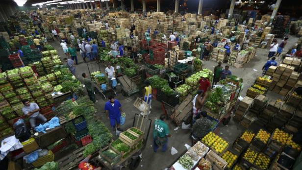Eine große Markthalle gefüllt mit Kisten voller Obst und Gemüse und vielen Menschen.