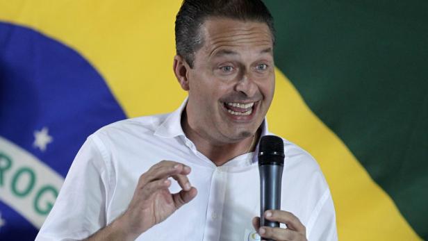 Ein Mann spricht vor einer brasilianischen Flagge in ein Mikrofon.