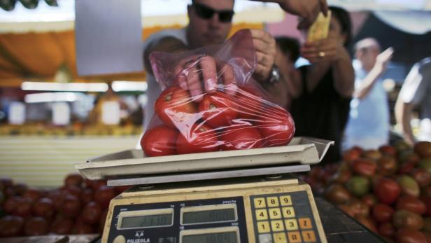 Ein Mann wiegt eine Tüte Tomaten auf einem Markt ab.