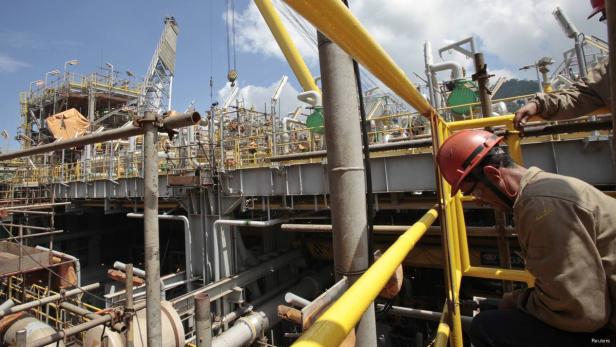 Ein Arbeiter mit Schutzhelm auf einer industriellen Anlage mit Rohren und Gerüsten.